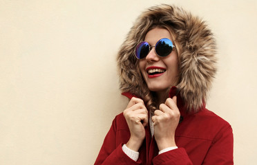 Portrait close up happy smiling young woman wearing red jacket with fur hood over background