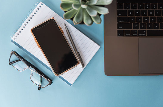 Overhead view of workspace with laptop, phone, glasses and notepad.