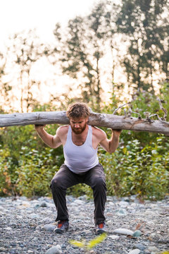 fit man prepares to shoulder press a log during an outdoor workout.