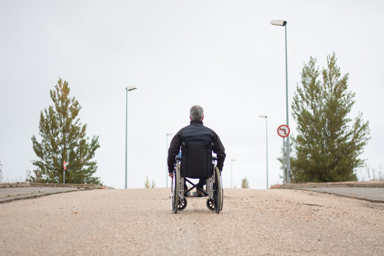 Rear vision of a disabled man in a wheelchair alone in the street