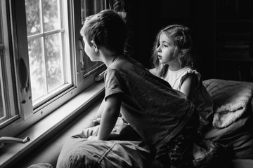 Two children perch on a couch and look out a window.