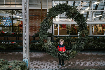 A little boy stands behind a huge wreath.