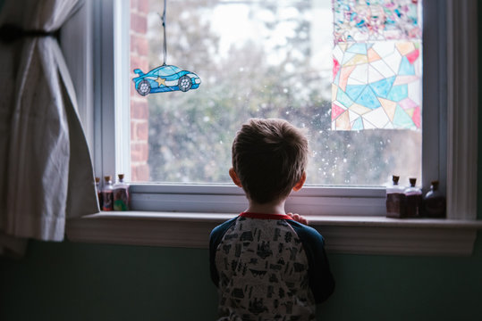 A Little Boy Looks Out A Window In His Bedroom.