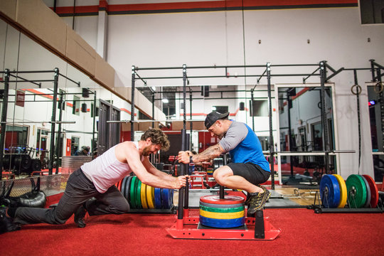 Personal trainer increasing weight on clients weight sled at gym.