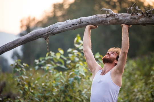 man shoulder presses a fallen tree outside in nature's gym.