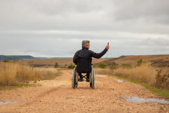 Rear vision of a disabled man in wheelchair in a path taking a selfie