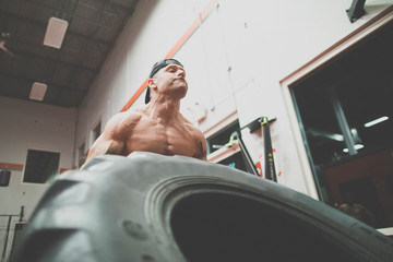 low angle view of muscular man lifts large tire at the gym