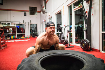 muscular man lifts large tire at the gym