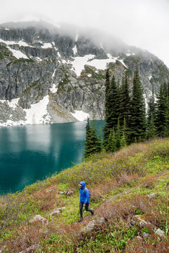 A woman hikes around a beautiful alpine lake on a cloudy, rainy summer day in the Coast Mountains around Pemberton, British Columbia.