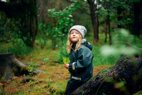 Small girl in hat and jacket sitting on tree stump and looking up