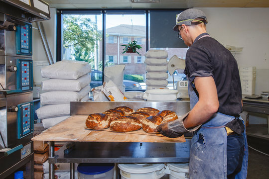 A professional baker sets tray of breads on counter in retail kitchen