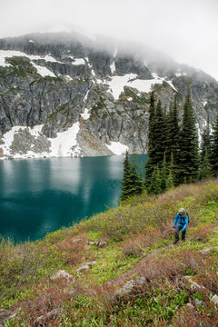 A man hikes around a beautiful alpine lake on a cloudy, rainy summer day in the Coast Mountains around Pemberton, British Columbia.