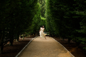 A young barefoot woman dances in a long white dress on tree-lined path