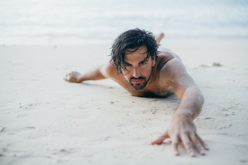 A handsome man lies on the sand by the ocean.