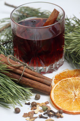 glass of mulled wine, cinnamon sticks, spice and orange chips with fir bough on white background close up. Vertical image, close up