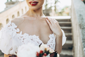 Wedding portrait of a bride, holding red and white flowers in hand. Close up, red lips, no face seen.