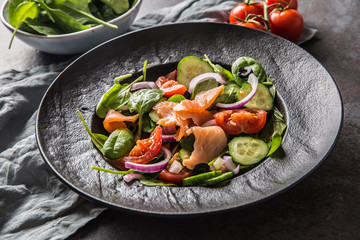 Salmon salad with vegetable in plate on dark kitchen table