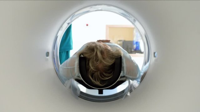 Close-up shot of a female mature patient lying on a table of CT scan machine. Computer tomograph scanning body and brain of elderly woman. High-tech equipment in medical clinic. 4K
