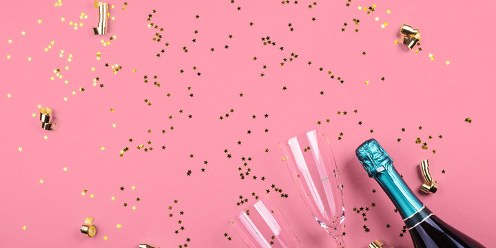 Two champagne glasses and bottle with golden star shaped confetti on pink color background. Celebrating new year, christmas, valentine's day festive flat lay. Anniversary, birthday party web banner