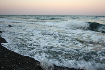 Sea waves crashing at sunset on the shore of the black, volcanic Kamari beach on the island of Santorini