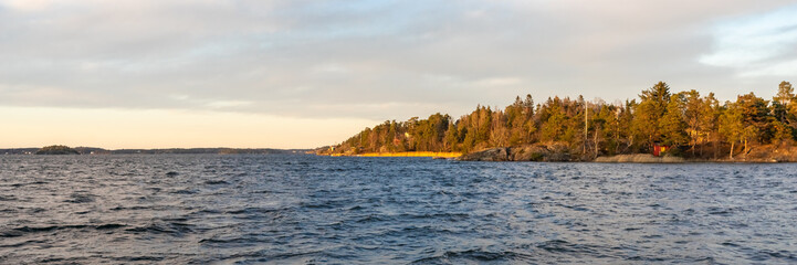 Seascape. Sunset background. Islands with pines in the rays of the setting sun. Stockholm Archipelago. Scandinavia. Seaside. Horizon line, skyline with beautiful clouds. Header.