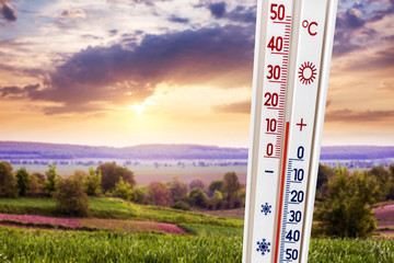 A thermometer against a background of a summer landscape at sunset shows 15 degrees of heat_