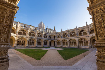 Obraz premium Empty inner courtyard between the ornamental cloisters at the historic Manueline style Mosteiro dos Jeronimos (Jeronimos Monastery) in Belem, Lisbon, Portugal, on a sunny day.