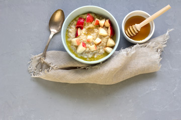 Breakfast, oatmeal porridge with butter and chopped red apples in a blue bowl, honey in a white bowl with a wooden honey spoon, cloth napkin, on a concrete background, free space, top view