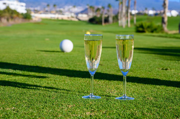 Two glasses with  bubbles white champagne or cava wine served on green golf club grass with mountains view during golf competition event or celebration
