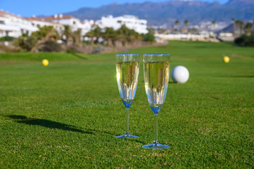 Two glasses with  bubbles white champagne or cava wine served on green golf club grass with mountains view during golf competition event or celebration