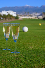 Two glasses with  bubbles white champagne or cava wine served on green golf club grass with mountains view during golf competition event or celebration