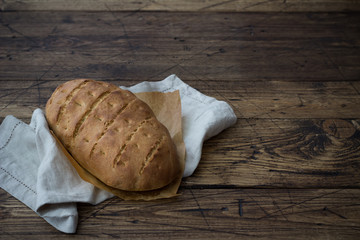 Homemade rustic bread on a textile napkin and aged dark wooden background, close up, free space