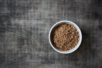 Buckwheat porridge in a white plate placed on a dark wooden background, close up, free space