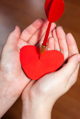 Red heart pierced by an arrow or dart in the palms. The concept of unsuccessful or broken love. Valentine's Day.