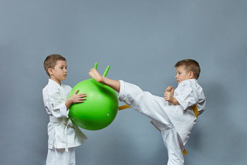Little athlete in white karategi kicks a green ball