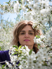 Fototapeta premium soft focus of attractive woman with long hair between blooming cherry branches with white flowers in garden in front of blue sky