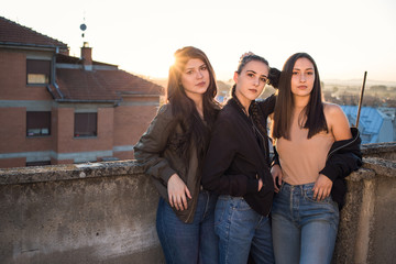 Three brunette teenage girls, friends standing on the rooftop in late afternoon.