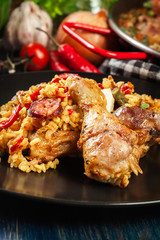 Traditional paella with chicken legs, sausage chorizo and vegetables served on black plate