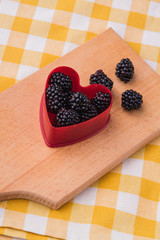 Obraz na płótnie Canvas Red plastic heart-shaped form with blackberries. Kitchen wooden board. Top view.