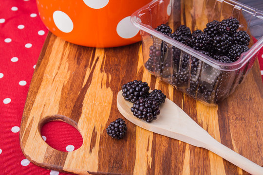 Fresh raw blackberries prepared for cooking jam. Wooden tablespoon and berries harvest on wooden board, top view.