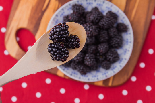 Wooden rural tablespoon above the plate of blackberries. Three berries in a spoon, top view.
