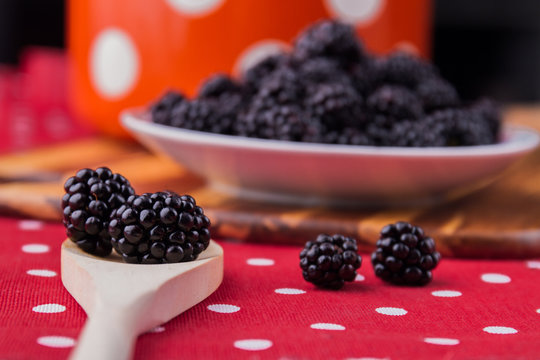 Wooden tablespoon with blackberries, close-up. Plate with berries background, cooking or eating concept.