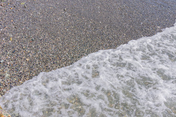 pebble coastline. Seashore with transparent water and small stones.