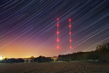 Star trails with transmitter towers in winter night. Starry sky with red lights.