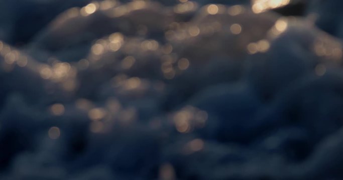 Blurred reflections of sunlight on the surface of waves covered with sea foam at sunset of summer day