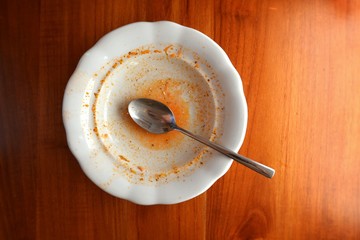 Empty white plate with spoon on wooden table, flat lay top view, red leftovers from soup or sauce