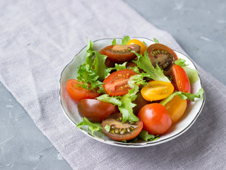 Fresh cherry tomatoes and salad in a white plate on a gray napkin.