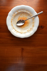 Empty white plate with spoon on wooden table, flat lay top view, red leftovers from soup or sauce
