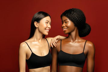 Multi Ethnic Group of beauty Womans with diffrent types of skin  together and looking on camera. Two Diverse ethnicity women -  African and Asian posing and smiling against red background.