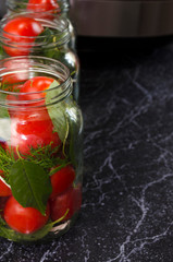 Canned vegetables on the marble table close-up. Tomatoes and cucumbers in the glass jars with copy space. Preserved food. Cooking process in the kitchen. Selective focus